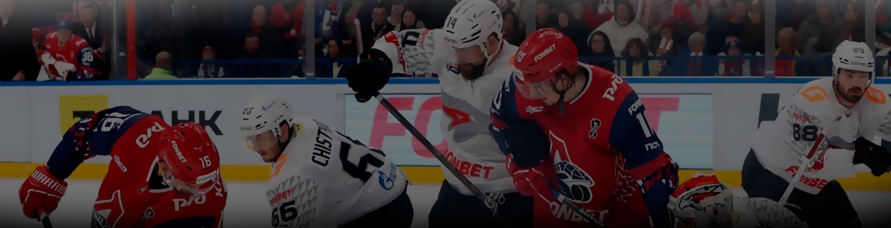На изображении хоккейный матч: игроки в красной и белой форме борются за шайбу на льду. На заднем плане видна трибуна с болельщиками. Атмосфера напряжённой игры
